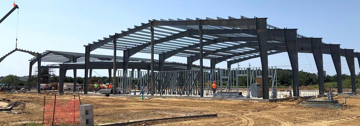 Steel frame of a pre-engineered metal building erected on a commercial site, with a crane and crew at work